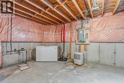 Unfinished below grade area with white refrigerator, electric panel, and drainage system - 