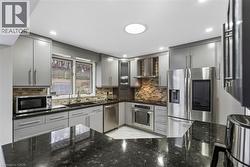 Kitchen with gray cabinetry, stainless steel appliances, dark stone counters, glass insert cabinets, and backsplash - 
