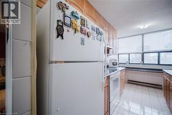 Kitchen featuring white appliances, a baseboard heating unit, a textured ceiling, wood finish cabinets, and light tile patterned floors - 