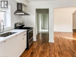 Second floor kitchen featuring electric stove, wood flooring, tasteful backsplash, white cabinetry, and light quartz countertops - 