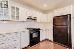 Main floor kitchen with black appliances, white cabinetry, glass insert cabinets, and recessed lighting - 