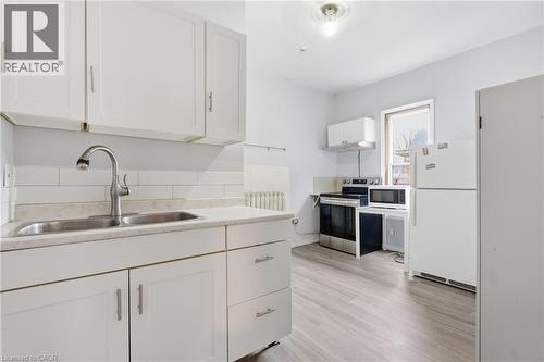 Kitchen with white appliances, light countertops, white cabinets, and light wood-style floors - 30 Regina Street N, Waterloo, ON 