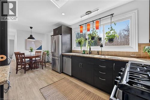 Kitchen featuring hanging light fixtures, light stone counters, stainless steel appliances, light wood-style floors, and dark cabinetry - 844 Upper Wellington Street, Hamilton, ON - Indoor Photo Showing Kitchen