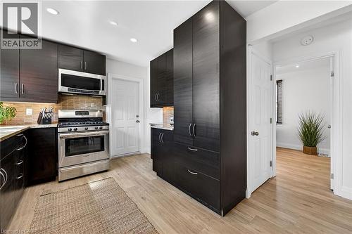 Kitchen with stainless steel appliances, light stone counters, light wood-type flooring, modern cabinets, and backsplash - 844 Upper Wellington Street, Hamilton, ON - Indoor Photo Showing Kitchen