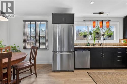 Kitchen with dark cabinetry, hanging light fixtures, stainless steel appliances, light wood-style flooring, and light stone countertops - 844 Upper Wellington Street, Hamilton, ON - Indoor