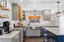 Kitchen with stainless steel appliances, dark wood-style floors, pendant lighting, light stone counters, and gray cabinetry - 