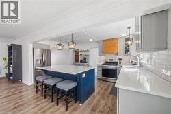 Two tone kitchen with hanging light fixtures, stainless steel appliances, a center island, a kitchen breakfast bar, and light wood finished floors - 