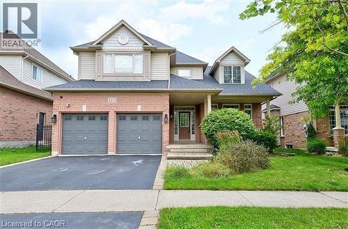 View of front of house featuring an attached garage, a porch, driveway, a front yard, and brick siding - 2215 Tiger Road, Burlington, ON - Outdoor With Facade