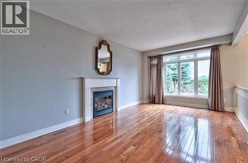 Unfurnished living room featuring light wood-type flooring, a glass covered fireplace, and a textured ceiling - 2215 Tiger Road, Burlington, ON - Indoor Photo Showing Living Room With Fireplace