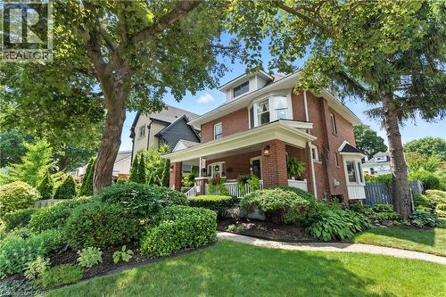 View of front facade featuring a porch, brick, and a front lawn - 98 Kensington Avenue S, Hamilton, ON - Outdoor With Deck Patio Veranda