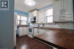 Kitchen with butcher block counters, white appliances, white cabinetry, decorative backsplash, and dark wood finished floors - 