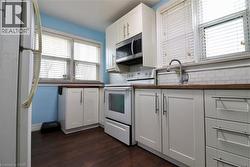 Kitchen with white appliances, white cabinets, dark wood finished floors, wooden counters, and decorative backsplash - 