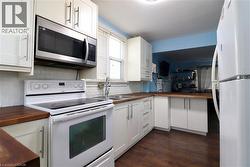 Kitchen featuring butcher block counters, white appliances, white cabinetry, and dark wood finished floors - 