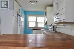 Kitchen with wooden counters, white cabinets, freestanding refrigerator, range with electric stovetop, and stainless steel microwave - 