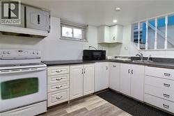Kitchen in basement with white range with electric stovetop, dark countertops, black microwave, light wood-style flooring, and recessed lighting - 