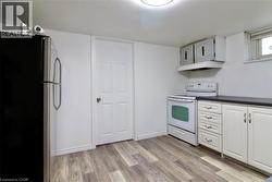 Kitchen in basement featuring freestanding refrigerator, electric stove, light wood finished floors, dark countertops, and white cabinetry - 