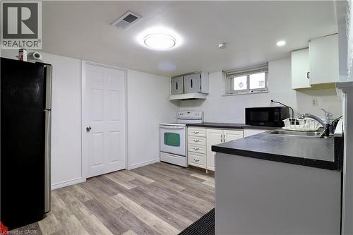 Kitchen in basement featuring electric range, freestanding refrigerator, dark countertops, black microwave, and light wood-type flooring - 80 Roseview Avenue, Cambridge, ON - Indoor Photo Showing Kitchen