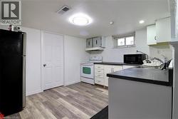 Kitchen in basement featuring electric range, freestanding refrigerator, dark countertops, black microwave, and light wood-type flooring - 