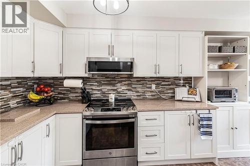 Kitchen featuring stainless steel appliances, white cabinets, light stone countertops, and tasteful backsplash - 311 Highway 8 Unit# 12, Stoney Creek, ON - Indoor Photo Showing Kitchen