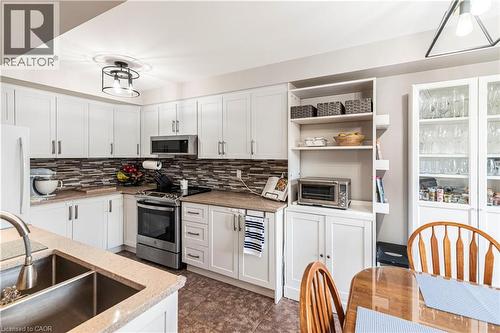 Kitchen featuring white cabinets, stainless steel appliances, light stone countertops, tasteful backsplash, and open shelves - 311 Highway 8 Unit# 12, Stoney Creek, ON - Indoor Photo Showing Kitchen With Double Sink