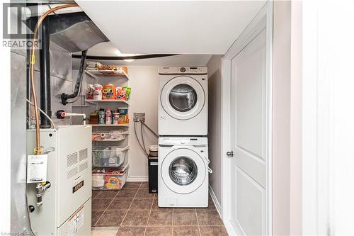 Laundry room featuring stacked washer / drying machine, heating unit, and dark tile patterned flooring - 311 Highway 8 Unit# 12, Stoney Creek, ON - Indoor Photo Showing Laundry Room