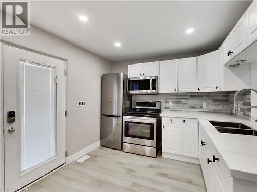 The property features a kitchen with white cabinetry, stainless steel appliances, and light-colored flooring - 229 Parkdale Avenue N, Hamilton, ON 