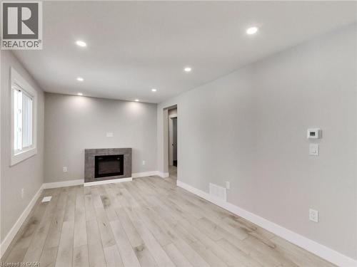 This living space features light-toned flooring, a fireplace with a stone-style surround, and recessed lighting - 229 Parkdale Avenue N, Hamilton, ON 