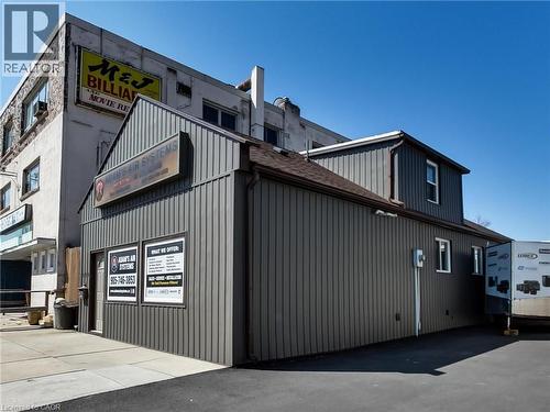 The property features a building with dark grey vertical siding and a brown roof - 229 Parkdale Avenue N, Hamilton, ON 