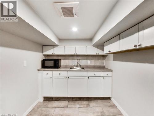 This area features white cabinetry with brushed nickel hardware, a neutral-toned countertop, and a stainless steel sink with a faucet - 229 Parkdale Avenue N, Hamilton, ON 