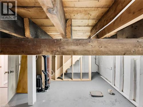 The property includes an unfinished basement space, featuring exposed wooden ceiling beams and a painted concrete floor - 229 Parkdale Avenue N, Hamilton, ON 