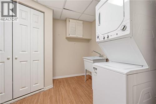 The property features a dedicated laundry area with a stacked washer and dryer, a utility sink, and wood-look flooring - 1 Tomahawk Drive, Grimsby, ON - Indoor Photo Showing Laundry Room
