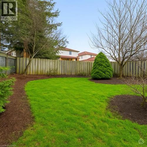 The property features a well-maintained lawn, a wooden fence, and mature trees - 1 Tomahawk Drive, Grimsby, ON - Outdoor With Backyard