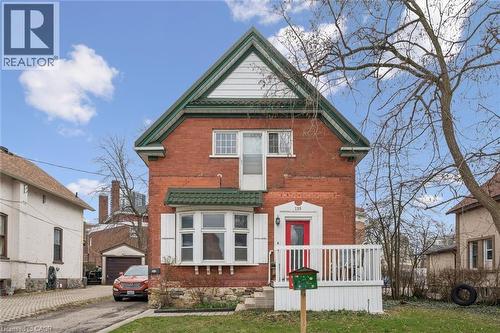 This property features a red brick exterior, a green metal roof accent, and a white front porch with railings - 155 Lancaster Street E, Kitchener, ON - Outdoor