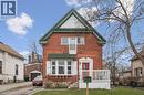 This property features a red brick exterior, a green metal roof accent, and a white front porch with railings - 155 Lancaster Street E, Kitchener, ON  - Outdoor 
