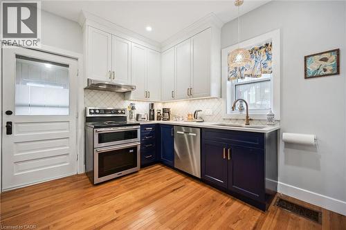 The kitchen features hardwood floors, white upper cabinetry, blue lower cabinetry, stainless steel appliances, and a window above the sink - 155 Lancaster Street E, Kitchener, ON - Indoor Photo Showing Kitchen