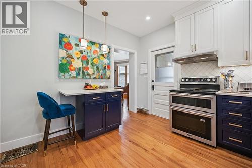 The kitchen features hardwood floors, white upper cabinetry, deep blue base cabinetry, stainless steel appliances, and pendant lighting - 155 Lancaster Street E, Kitchener, ON - Indoor Photo Showing Kitchen