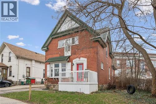 The property features a red brick exterior with white trim and a green roof, complemented by a white porch and a distinctive red front door - 155 Lancaster Street E, Kitchener, ON - Outdoor