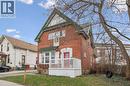 The property features a red brick exterior with white trim and a green roof, complemented by a white porch and a distinctive red front door - 155 Lancaster Street E, Kitchener, ON  - Outdoor 