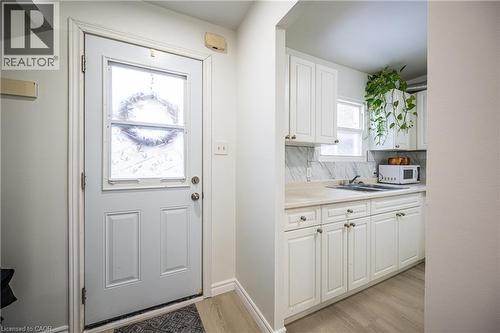The entrance features a door with a decorative glass insert, leading directly into a kitchen area with white cabinetry, a sink, and a window - 212 Westcourt Place, Waterloo, ON - Indoor