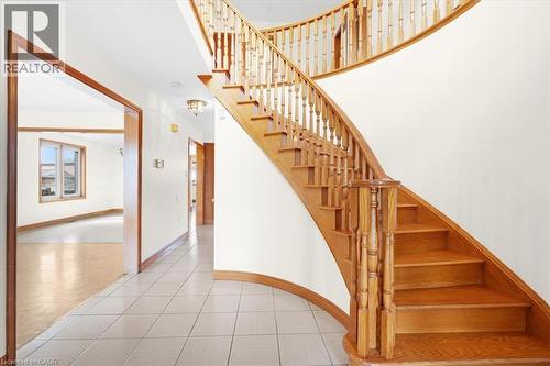 The property features a grand wooden staircase with ornate balusters, a tiled entryway, and an interior hallway with light-colored flooring - 18 Marcel Place, Hamilton, ON - Indoor Photo Showing Other Room