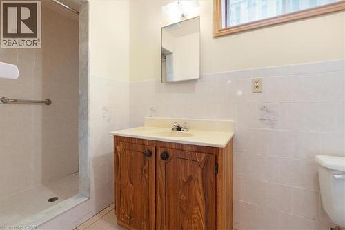 Bathroom featuring a wooden vanity with a light-colored countertop and an integrated sink, a rectangular mirror, and a shower with a grab bar - 18 Marcel Place, Hamilton, ON - Indoor Photo Showing Bathroom