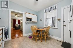 The kitchen features light-colored flooring, white cabinetry with wood trim, and a window with striped curtains - 
