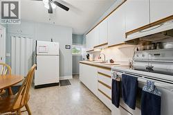 The kitchen features white cabinetry with wood trim, a white electric range, a white refrigerator, and a ceiling fan - 