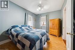 This room features light wood laminate  flooring, a ceiling fan with integrated lighting, and two windows with blinds and patterned curtains - 