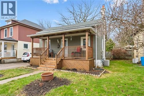 The property features a charming front porch with wooden railings and steps, set on a grassy yard with a concrete pathway leading to the entrance - 28 Davidson Street, Cambridge, ON - Outdoor With Deck Patio Veranda