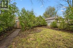 Expansive yard featuring a lawn area, mature trees, and a paved pathway leading to a wooden shed - 