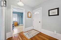 Inviting entrance featuring hardwood floors, a white entry door with an arched window, and a light fixture - 