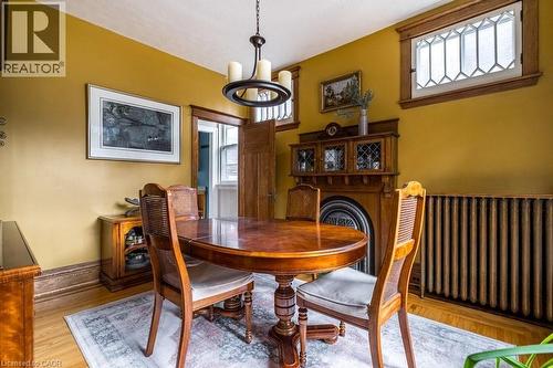 This room features hardwood floors, a prominent wooden fireplace surround with an integrated cabinet, and decorative windows with intricate leaded glass patterns - 36 Eastbourne Avenue, Hamilton, ON - Indoor Photo Showing Dining Room