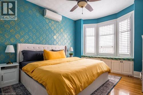 This room features hardwood floors, a ceiling fan, and bay windows with white plantation shutters - 36 Eastbourne Avenue, Hamilton, ON - Indoor Photo Showing Bedroom