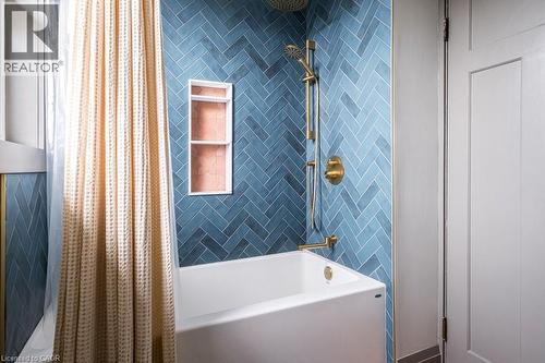 Bathroom featuring a white bathtub, blue herringbone tile shower surround, and gold-toned shower fixtures - 36 Eastbourne Avenue, Hamilton, ON - Indoor Photo Showing Bathroom